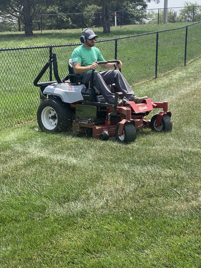 A lawn care worker mowing a sloped residential yard with a riding mower for Heath's Lawn Care in Omaha, NE.
