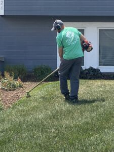 A lawn care worker trimming grass edges with a string trimmer for Heath's Lawn Care in Omaha, NE.