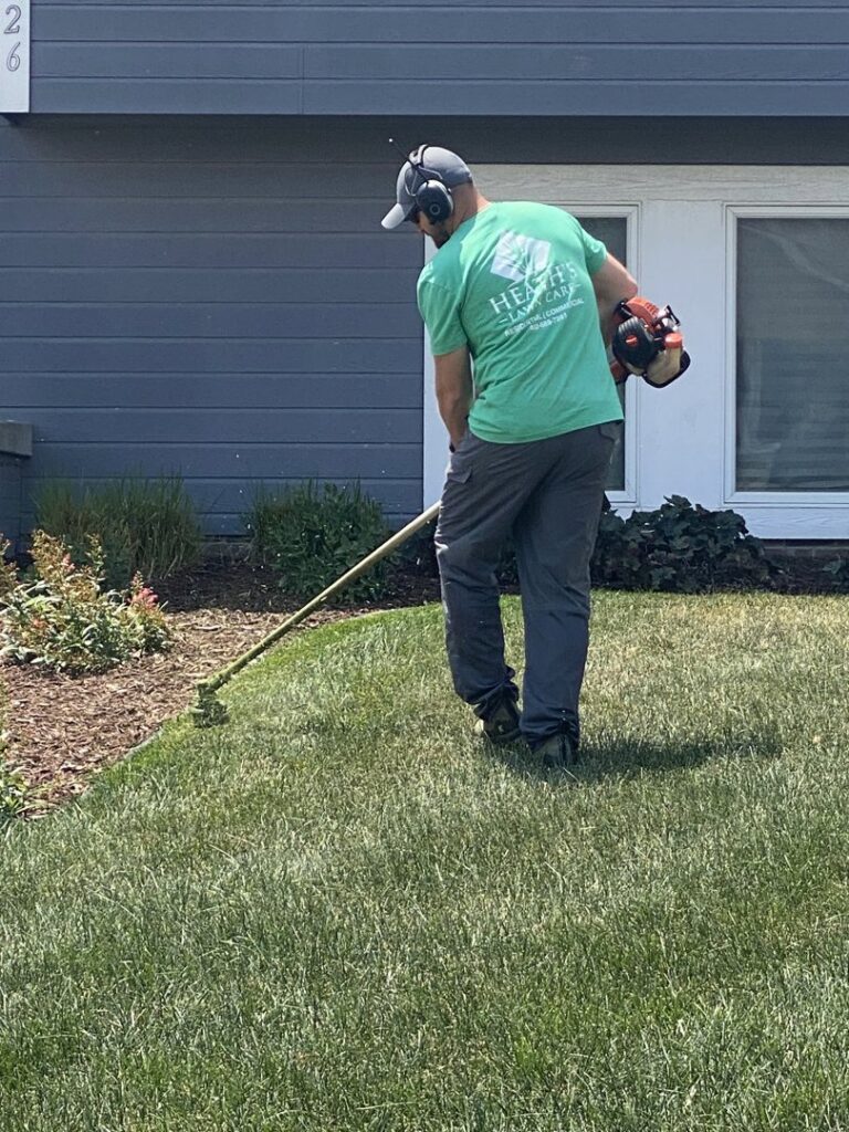 A lawn care worker trimming grass edges with a string trimmer for Heath's Lawn Care in Omaha, NE.