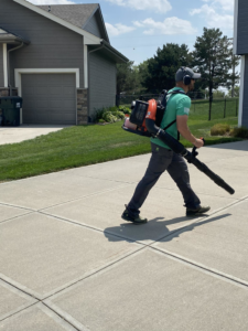 A lawn care worker carrying a backpack leaf blower on a driveway for Heath's Lawn Care in Omaha, NE.