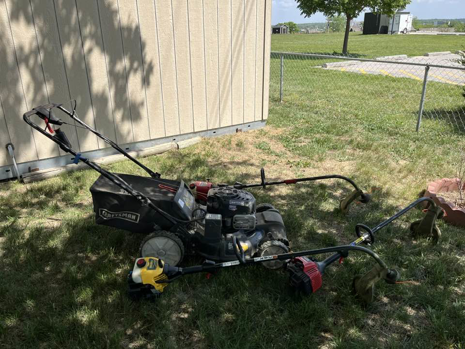 A push lawnmower and multiple string trimmers laid out on a lawn by Bucks Lawn Care LLC in Lincoln, NE.