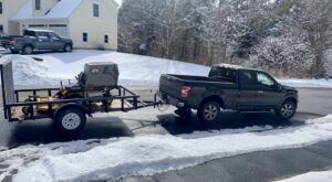 A professional riding lawn mower loaded on a trailer, towed by a pickup truck for Steele Lawns in Portland, ME.