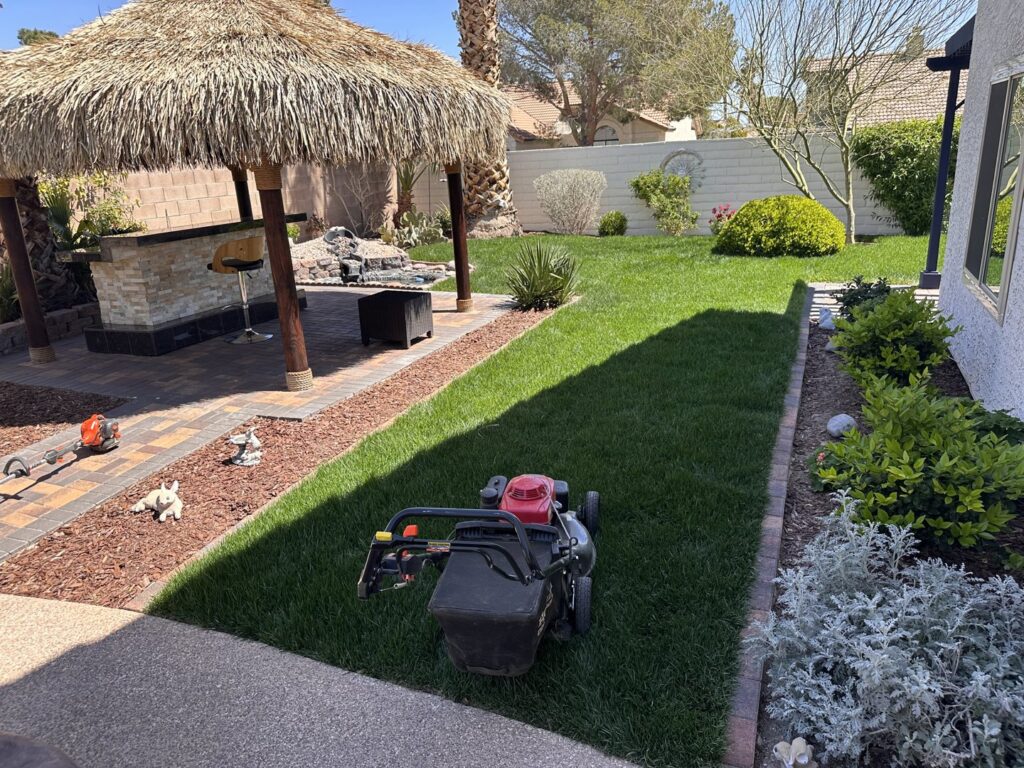 A lawnmower ready for or just finished mowing a lush green backyard lawn by Jireh landscaping and maintenance in Henderson, NV