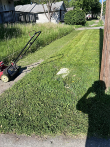 A lawnmower on a sidewalk next to a partially mowed lawn by Vick's Lawn Care Service in Des Moines, IA.