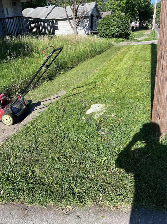 A lawnmower on a sidewalk next to a partially mowed lawn by Vick's Lawn Care Service in Des Moines, IA.