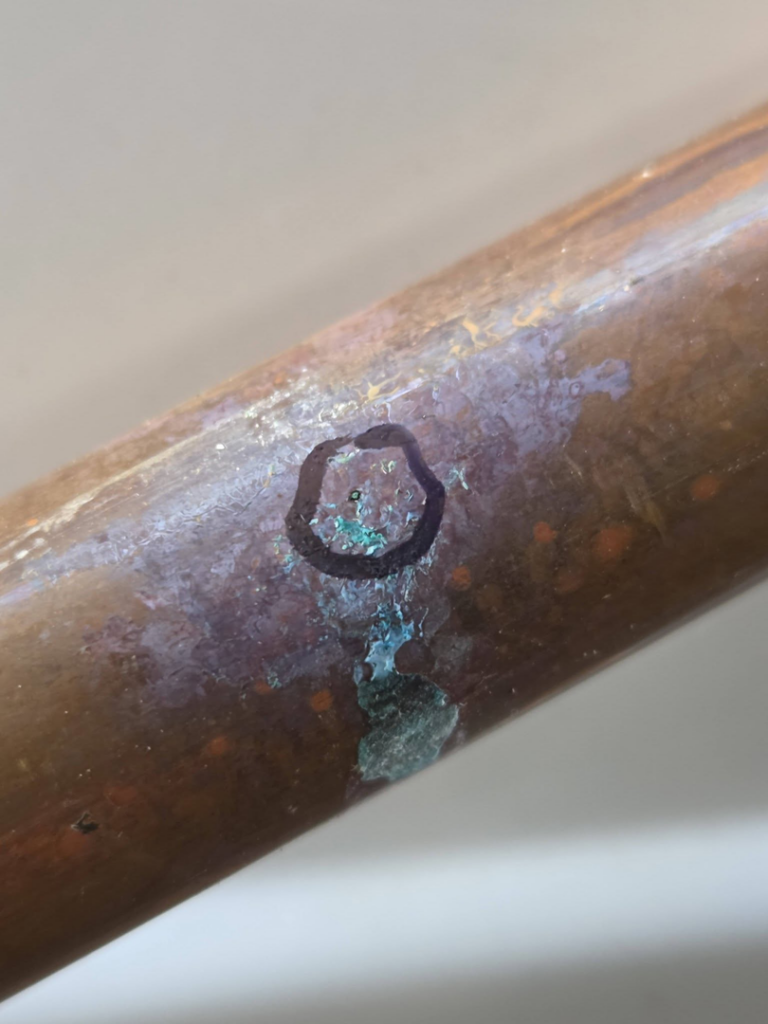 A close-up of a leaking copper pipe with corrosion, indicating water damage, by Freestone Plumbing in Corvallis, OR