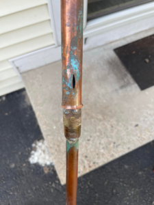 A close-up of a damaged copper pipe with a visible leak, a common source of water damage that The Restoration Experts in Waupaca, WI can address.