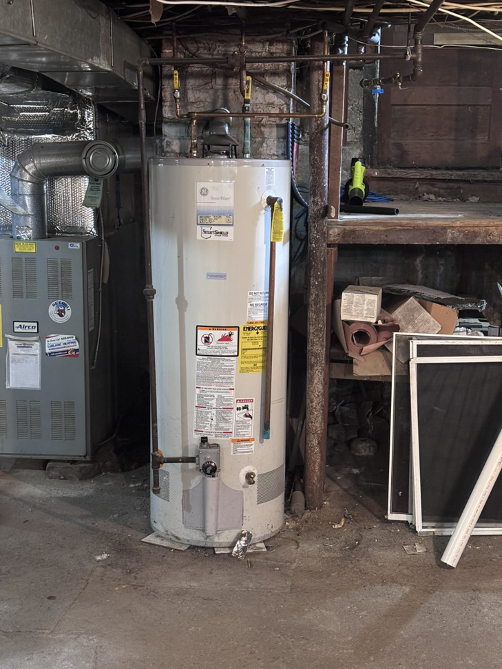 An old water heater showing signs of leakage and water damage in a basement, serviced by White Birch Plumbing in Derry, NH.