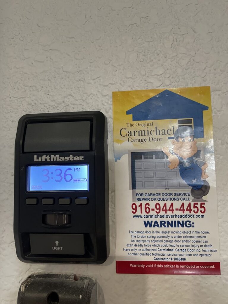 A LiftMaster garage door control panel next to a Carmichael Garage Door service sticker, indicating professional installation and service in Carmichael, CA.