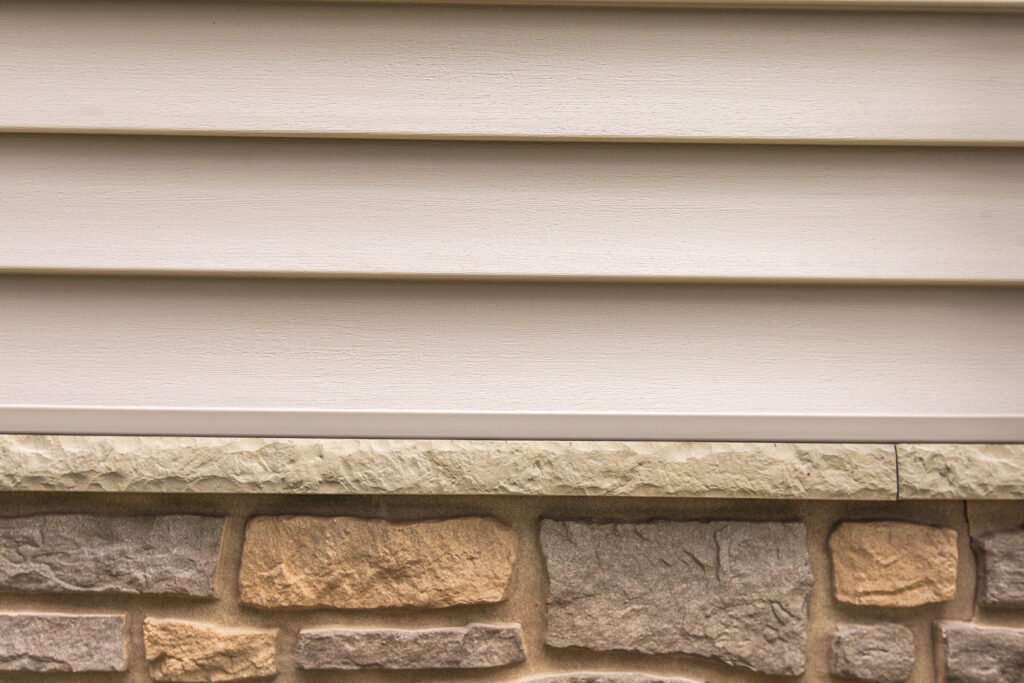 A detailed view of light beige horizontal siding above a stone foundation, installed by A&D Exteriors in Naperville, IL.