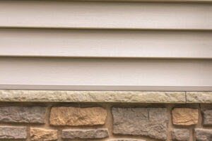 A detailed view of light beige horizontal siding above a stone foundation, installed by A&D Exteriors in Naperville, IL.