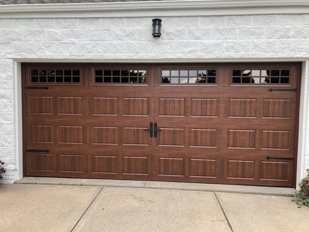 Two light-colored garage doors with arched windows and decorative handles installed by JLM Garage Doors Omaha in Papillion, NE.
