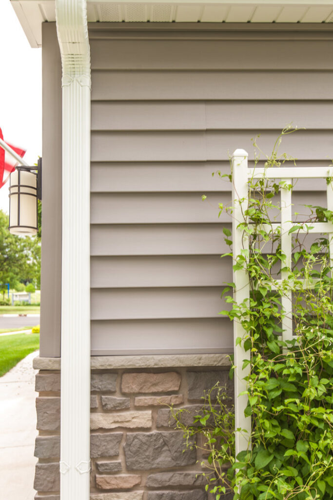 A close-up of light gray horizontal siding above a stone foundation, installed by A&D Exteriors in Naperville, IL.