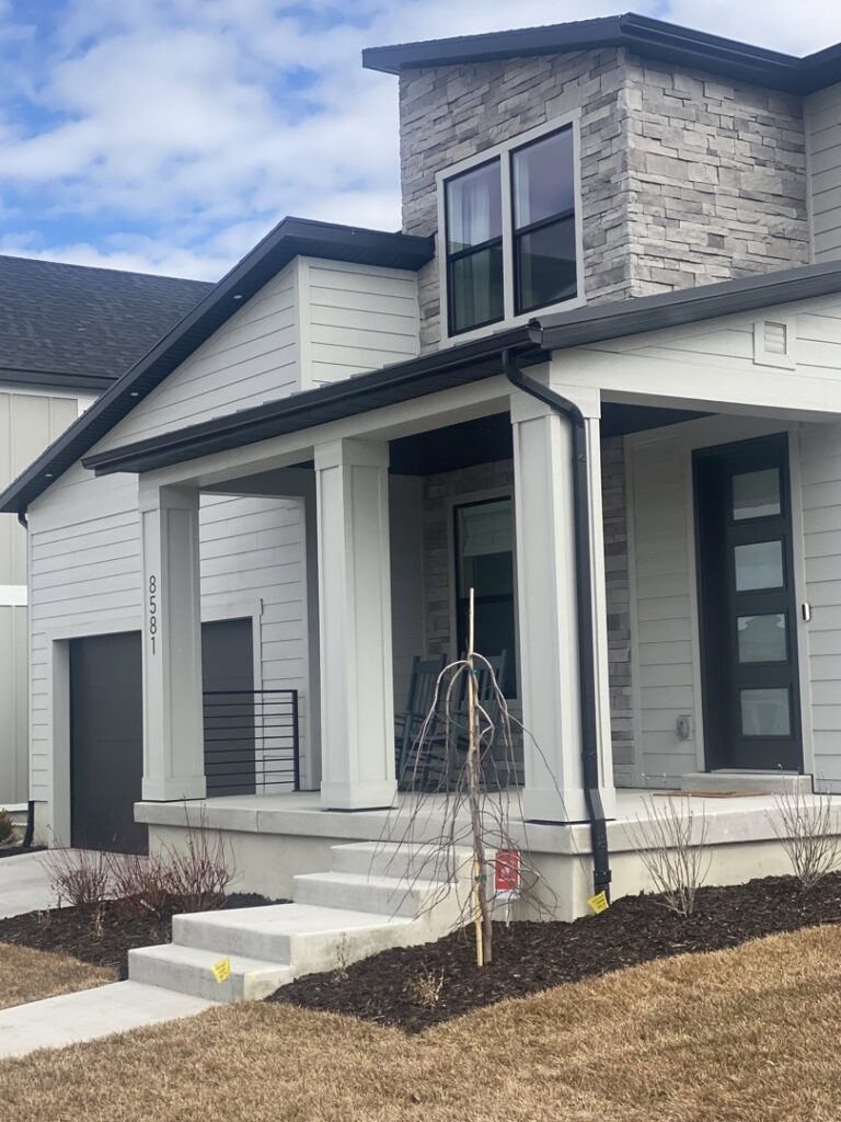 A modern home featuring light gray horizontal siding and elegant stone accents, completed by New Look Siding in Midvale, UT.