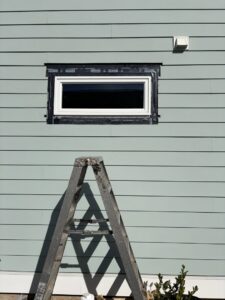Close-up of light green horizontal siding installation around a window with a ladder, by Powell Roofing in Ladson, SC.
