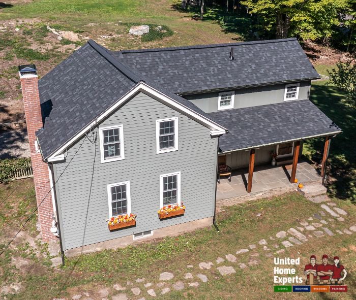 A charming light green house with new siding and a dark roof, completed by United Home Experts in Ashland, MA