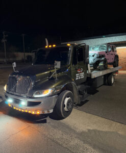 A light-colored Jeep loaded onto a flatbed tow truck from Bullcity Towing & Services LLC at night in Durham, NC.