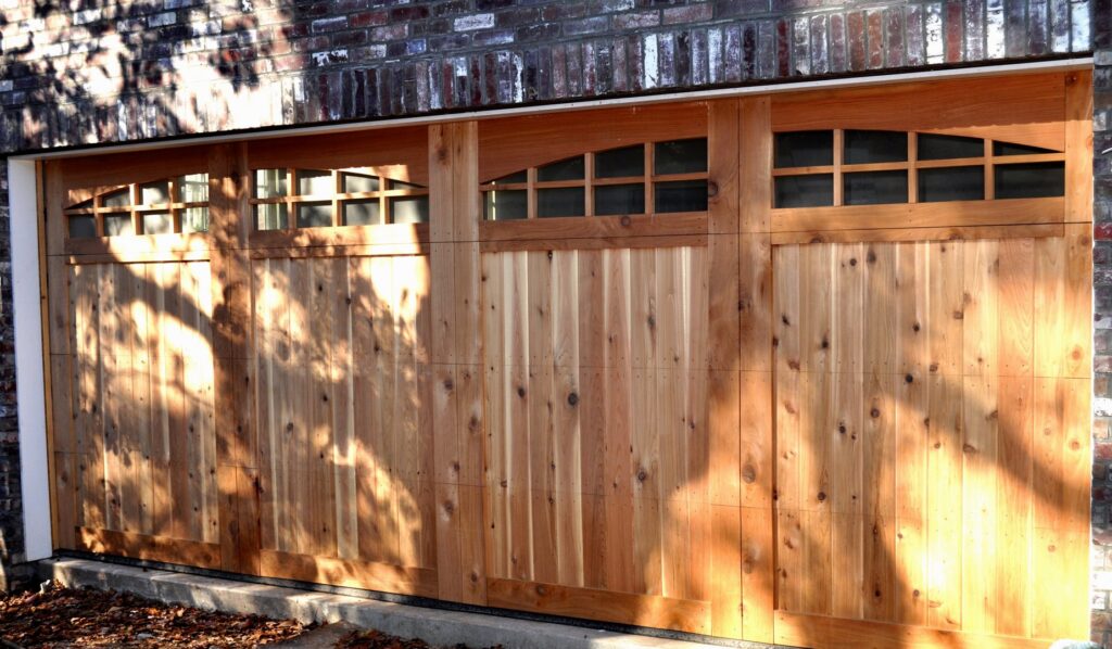 A light wood garage door with arched windows installed on a brick house by Coney's Garage Doors in Conway, AR.