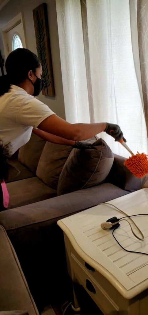A house cleaner dusting curtains in a living room for TAG Team Cleaning of West Hartford, CT