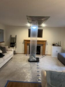 A living room set up for drying with plastic sheeting and a large air mover after water damage by Harbaugh Restoration in Vancouver, WA.