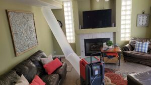 Professional drying equipment, including a large air duct and dehumidifier, set up in a living room for water damage restoration by Utah Disaster Team in Layton, UT.
