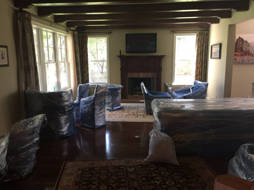 A living room with furniture carefully wrapped in blue moving blankets and plastic by TruMoving in Lakewood, CO.