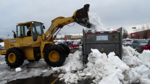 A yellow loader dumping snow into a large container in a parking lot for Snow & Ice Management Company in Pittsburgh, PA.