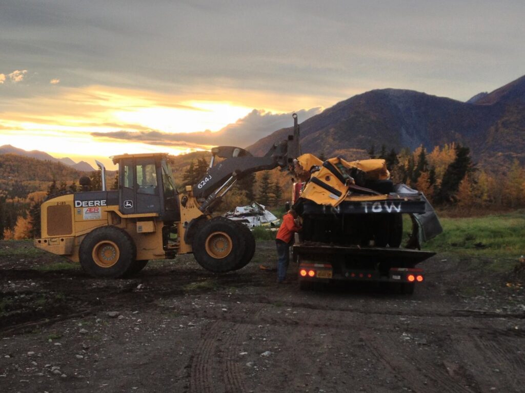 A front-end loader loading a crushed car onto a tow trailer for AK Car Crushing & Recycling & ACCR Towing in Wasilla, AK.