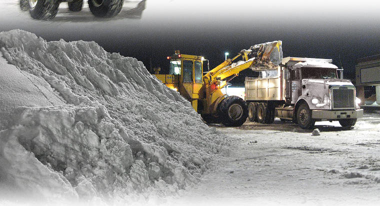 A front-end loader efficiently loading a large pile of snow into a dump truck for hauling by Appleton Snow Removal in Appleton, WI.