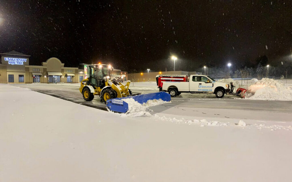 A loader and a pickup truck plowing snow in a commercial parking lot at night for Snow & Ice Management Company in Pittsburgh, PA.