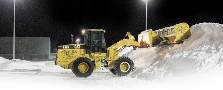 A yellow CAT loader pushing a large pile of snow at night for Snow & Ice Management Company in Pittsburgh, PA.
