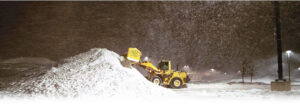 A yellow loader pushing a large snow pile while snow falls at night for Snow & Ice Management Company in Pittsburgh, PA.