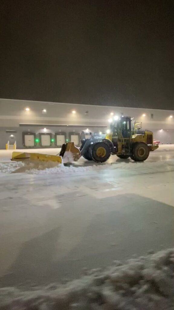A large front-end loader with a plow attachment actively clearing snow at night for Turf Pro Lawn Care & Snow Removal in Green Bay, WI.