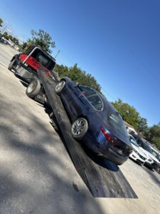 A blue sedan being loaded onto a flatbed tow truck by Rodicio Towing Services in Hialeah, FL.