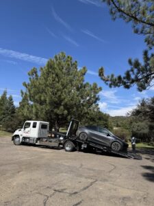 A Pacific Autow Center tow truck worker loading a grey Tesla Model Y onto its flatbed in San Diego, CA.