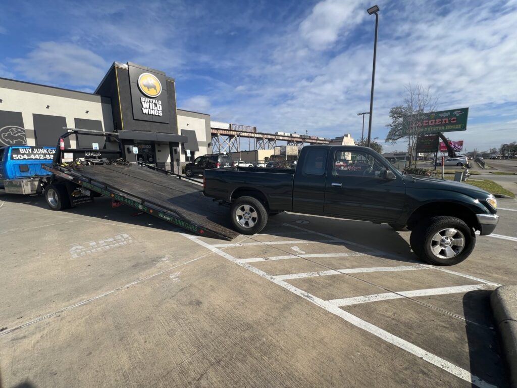 A dark green Toyota Tacoma pickup truck being loaded onto a flatbed tow truck by ABOD Towing LLC in New Orleans, LA.