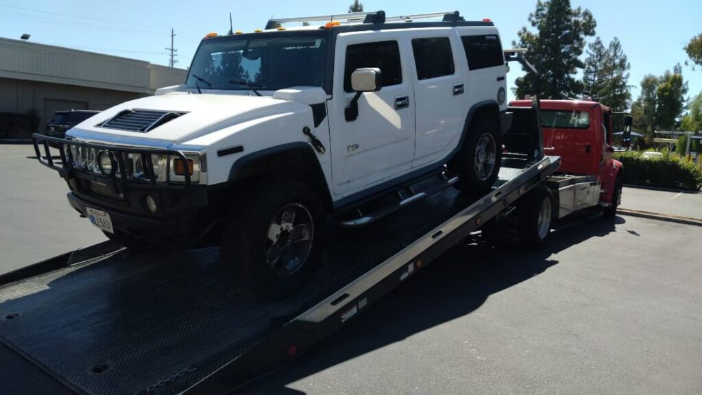 A white Hummer H2 SUV being loaded onto a flatbed tow truck by 101 auto towing inc in San Jose, CA.