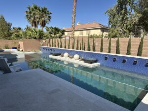 A long swimming pool featuring blue mosaic tiling and elegant water features by Greencare.net POOL Builder in Las Vegas, NV