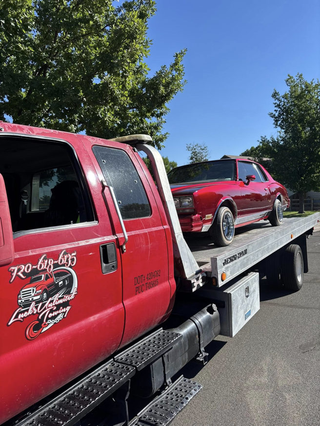 The red tow truck of Luck's Unlimited Towing with its logo, transporting a classic car in Thornton, CO.