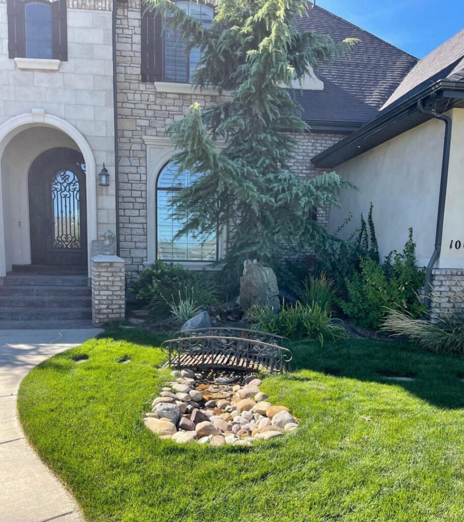 A lush green lawn with a decorative bridge and rock landscaping at a home by M.D. Lawn Care & Landscaping in West Jordan, UT