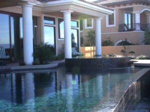 A luxurious pool with a dark bottom or infinity edge reflecting a grand home, built by Steve Breck Pools in Las Vegas, NV.