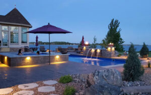 A luxurious illuminated pool and spa area with water features and fire bowls by Backyard Escapes by Kerner Pools & Spas in Bismarck, ND.