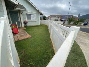 A well-maintained front yard with green grass and a white picket fence, cared for by LTN Yard Services LLC in Kaneohe, HI.