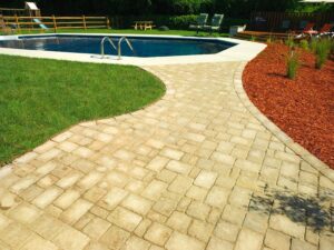 A neatly maintained strip of green grass alongside a paved pathway and swimming pool by Bailey's Lawn and Landscape in Smyrna, DE.