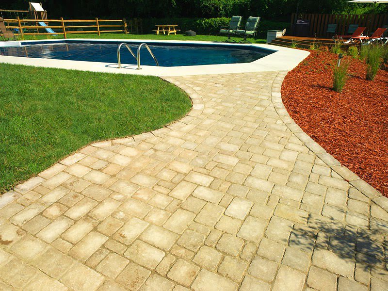 A neatly maintained strip of green grass alongside a paved pathway and swimming pool by Bailey's Lawn and Landscape in Smyrna, DE.