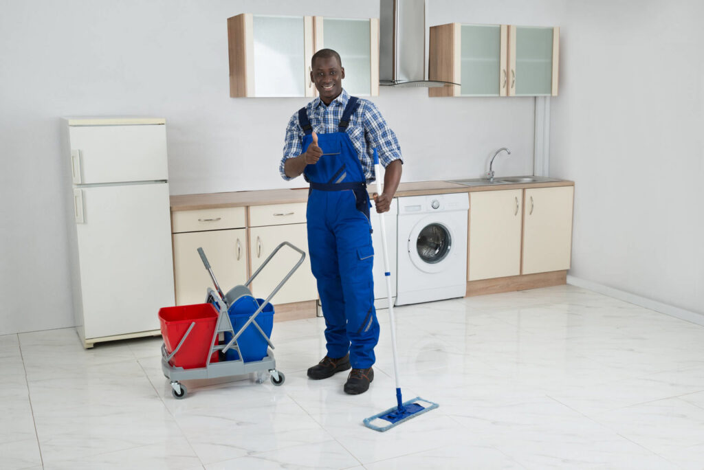 A male cleaner mopping a kitchen floor, giving a thumbs up, for Core Needs Janitorial in Indianapolis, IN.