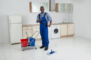 A male cleaner mopping a kitchen floor, giving a thumbs up, for Core Needs Janitorial in Indianapolis, IN.