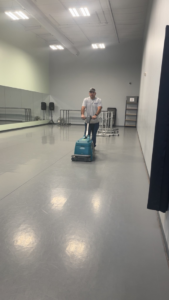 A man professionally cleaning a large floor with a scrubbing machine for Elite Cleaning of Des Moines, IA