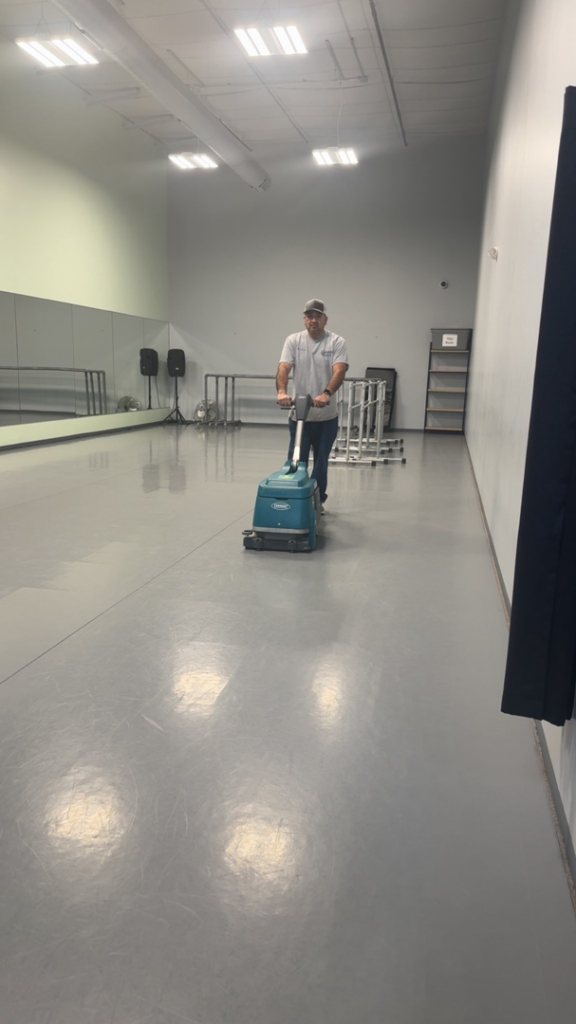 A man professionally cleaning a large floor with a scrubbing machine for Elite Cleaning of Des Moines, IA
