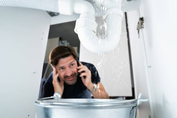 A man looking distressed by a leaking sink and water damage, calling for help from Olive Branch Plumbing Co in Olive Branch, MS.